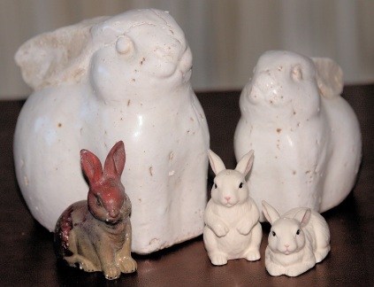 five mixed sizes of ceramic bunnies ranging from 2 1/2 to 12 inches high. One is brown with read burned into it